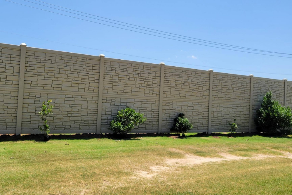 Composite fencing looks like stone wall with small bushes lining the edge.