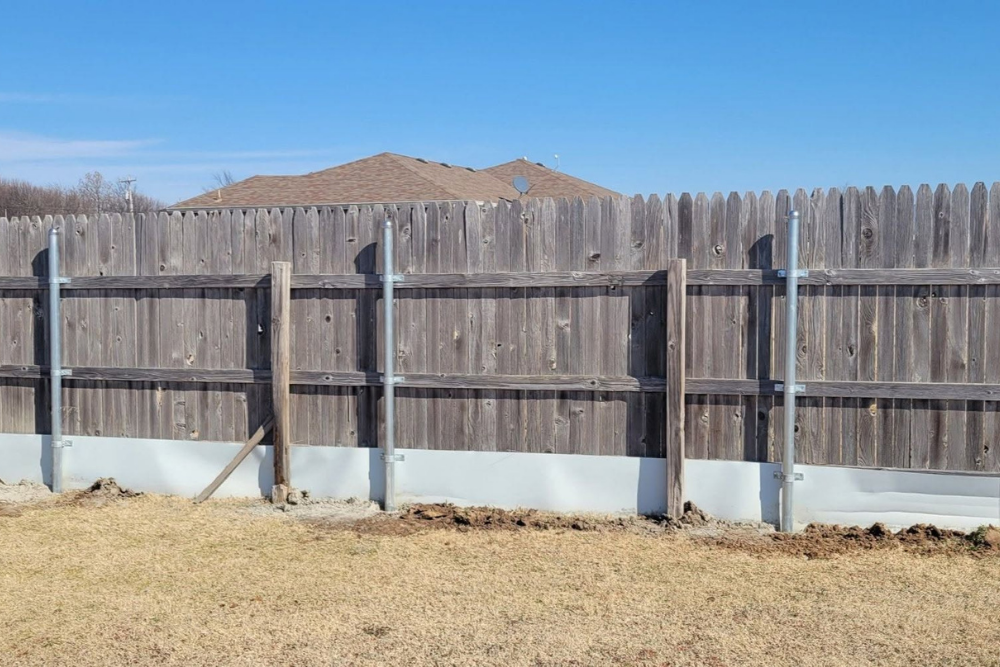 Wooden privacy fence, repaired with metal pole reinforcements.