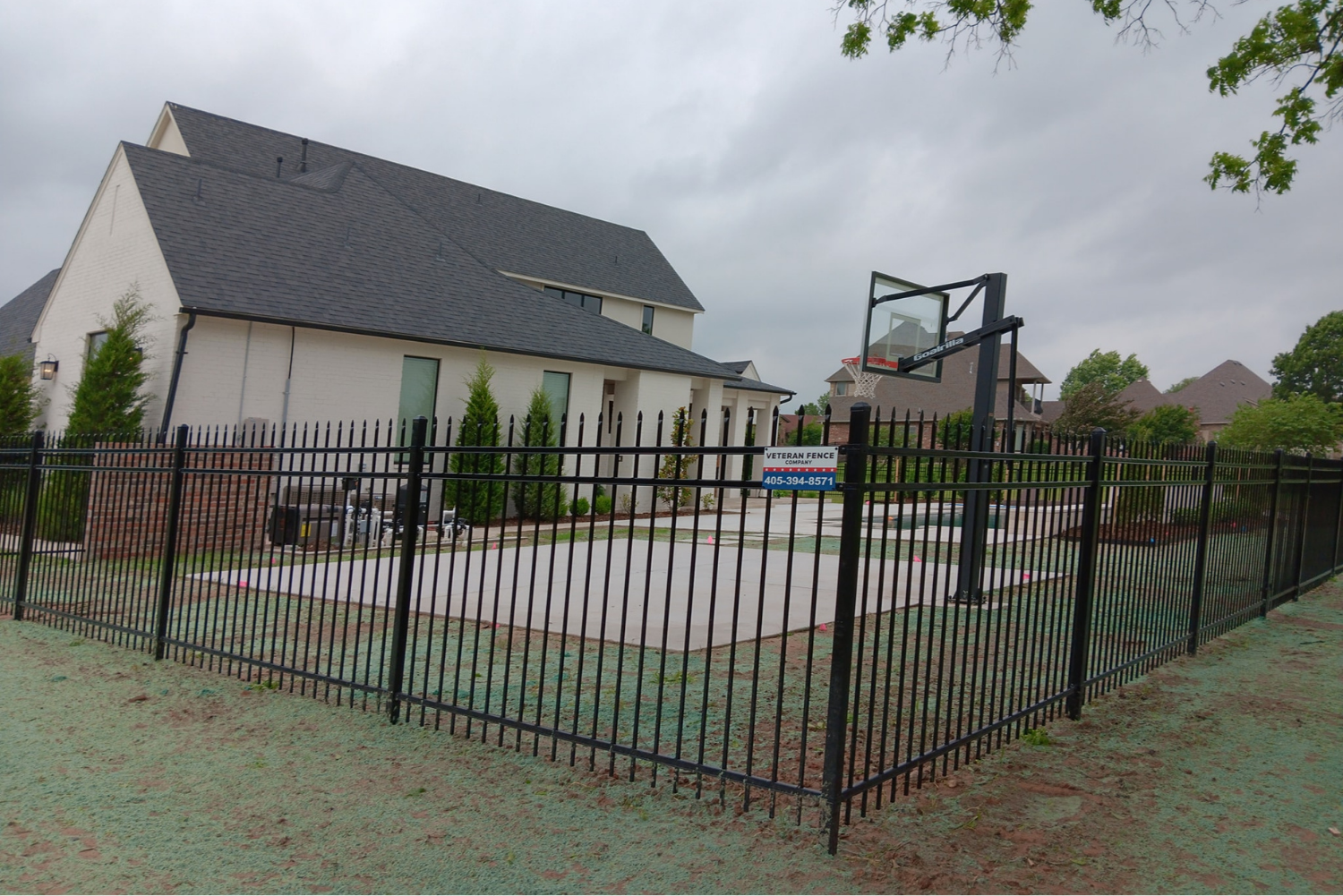 Iron ornamental fence surrounds basketball goal near residential home.